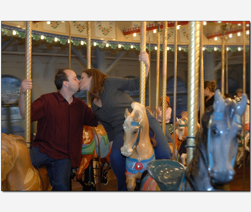 engaged couple kissing on a carousel